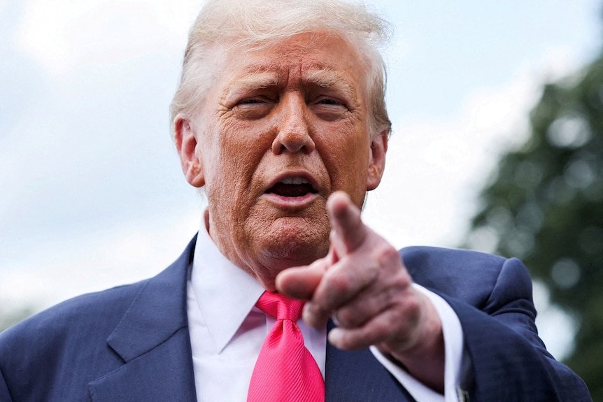A man in a suit points at the camera